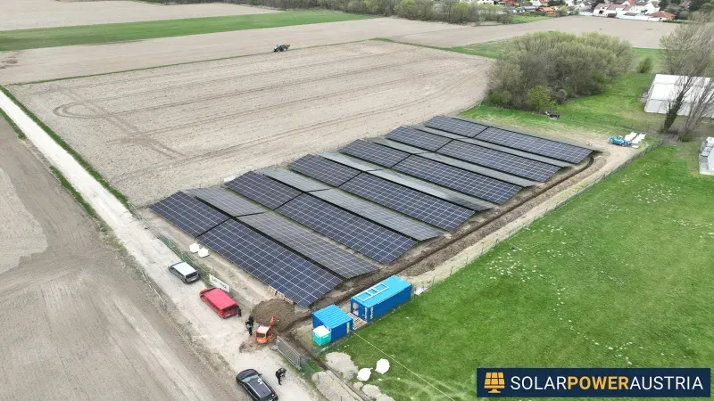 Luftaufnahme mehrerer Modulreihen einer Photovoltaik-Freiflächenanlage entlang eines Feldwegs