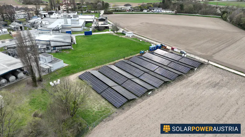 Luftaufnahme einer Photovoltaik-Freiflächenanlage neben einem Betriebsgelände und einem Sportplatz
